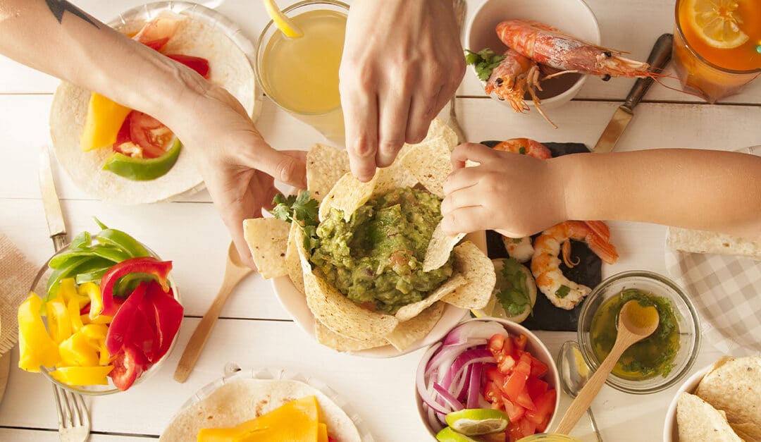 Mexican food on table with hands of woman and child dipping chips in guacamole
