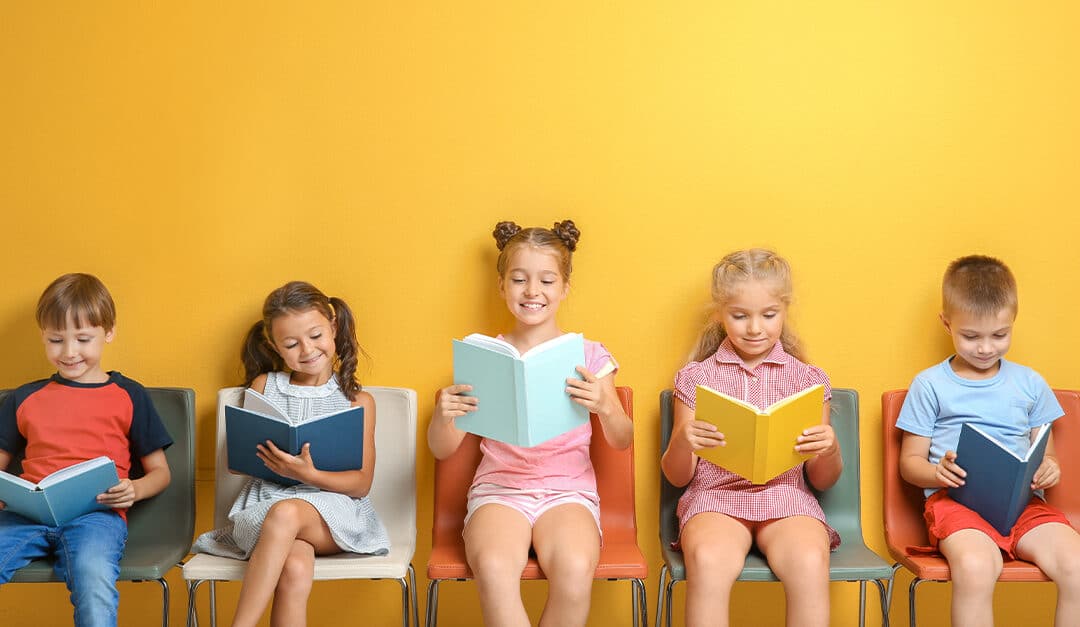 Cute little children reading books while sitting near yellow wall
