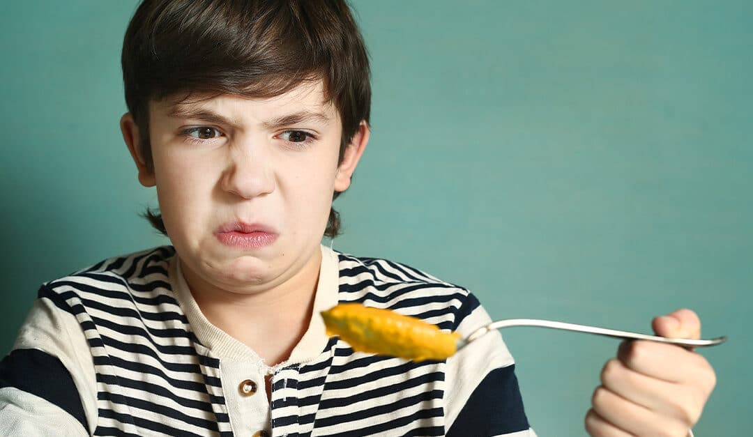 Preteen boy with tablespoon of pumpkin soup refuse to eat disgust grimace