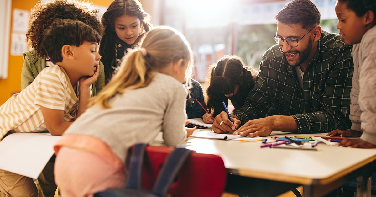 Group of elementary school kids stand around a table in a classroom, attentively following a lesson being taught by their teacher. Young students engaging in a fun activity of colouring and drawing.