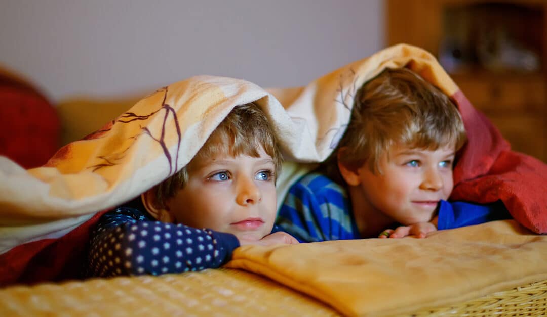 Happy little brothers, adorable kid boys watching television while lying on couch with blanket over the top of their heads. Learn Spanish while watching Paw Patrol