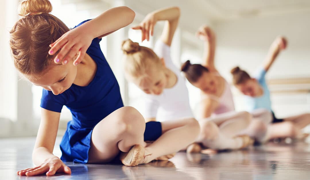 Little ballerinas doing exercises and bending sitting on floor in ballet class.