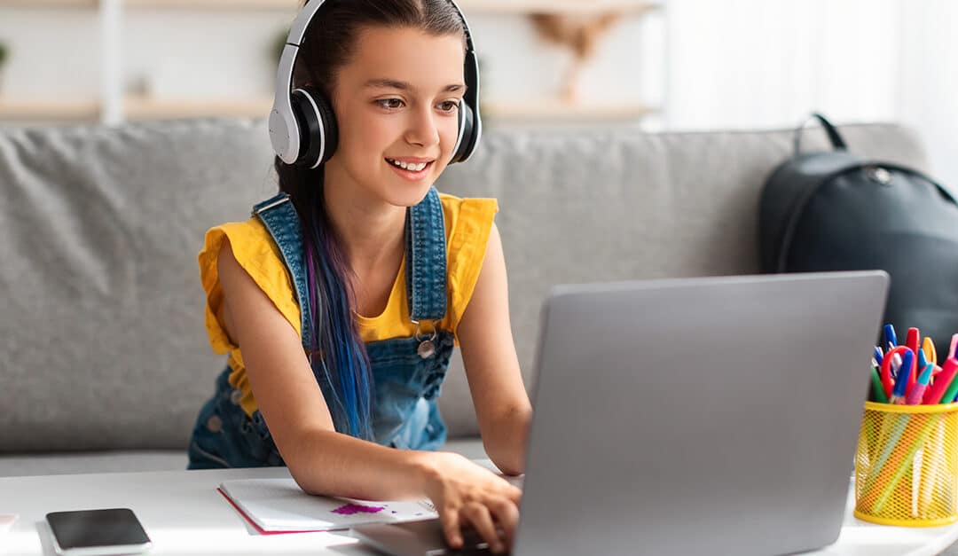 Portrait of young girl in wireless headset using laptop, studying Spanish online at home, typing on keyboard looking at pc screen