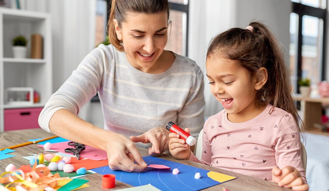 Mother spending time with her little daughter with glue making applique of color paper at home, printable crafts