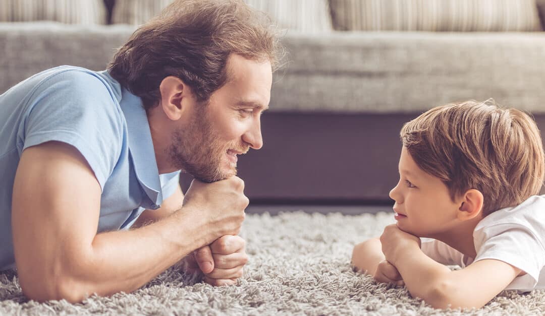 Side view of father and son lying on the floor and looking at each other and smiling while spending time together at home