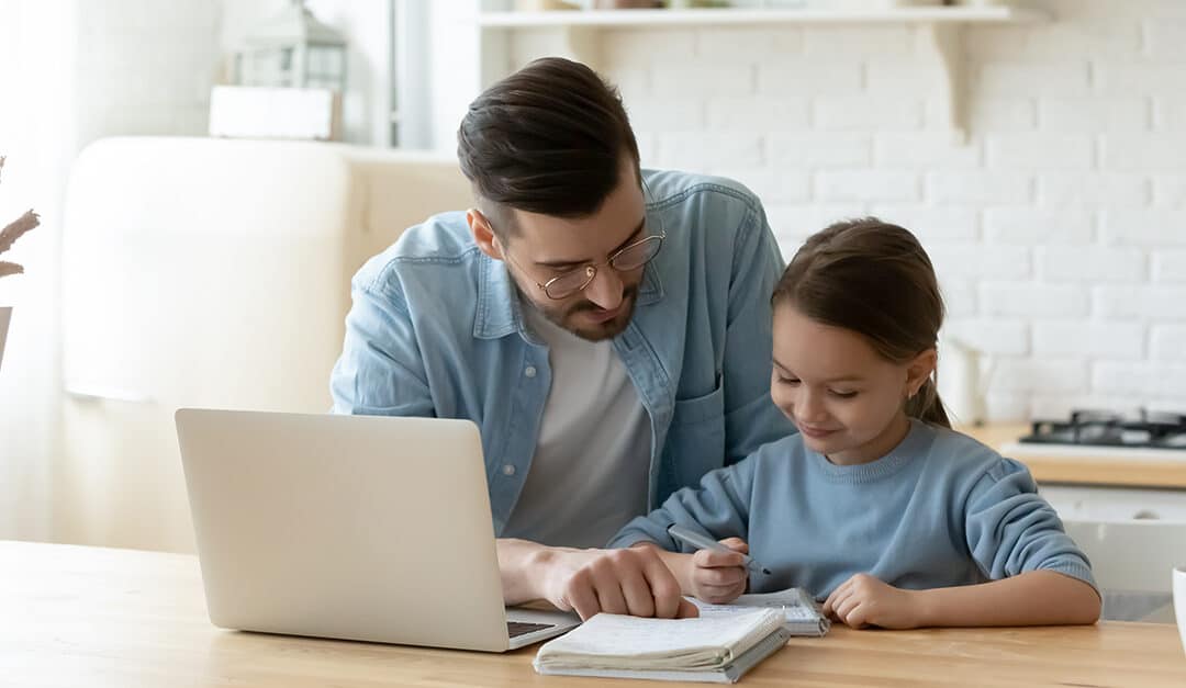 Father and daughter sitting at a table with a laptop and homework