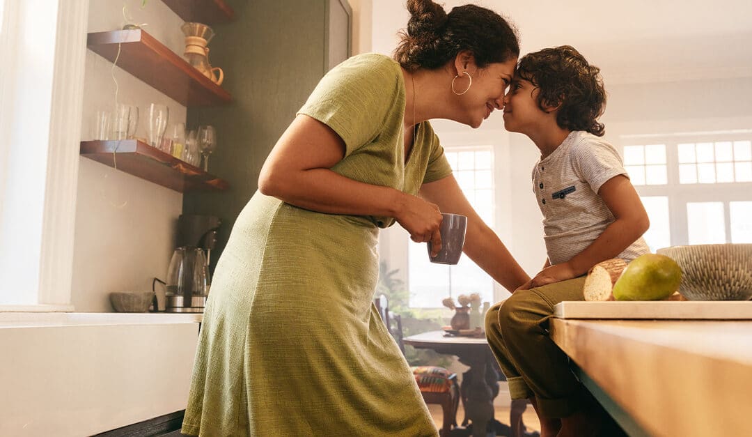 Affectionate mother touching noses with her young son in the kitchen.