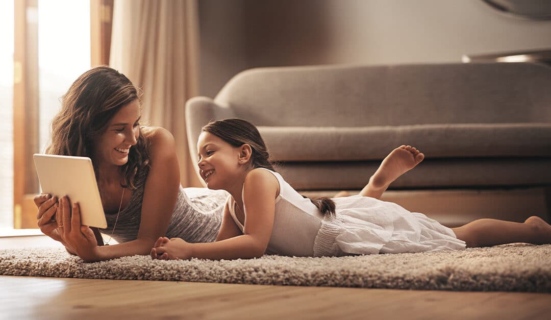 Mom and daughter looking at a tablet while laying on living room floor, learning Spanish