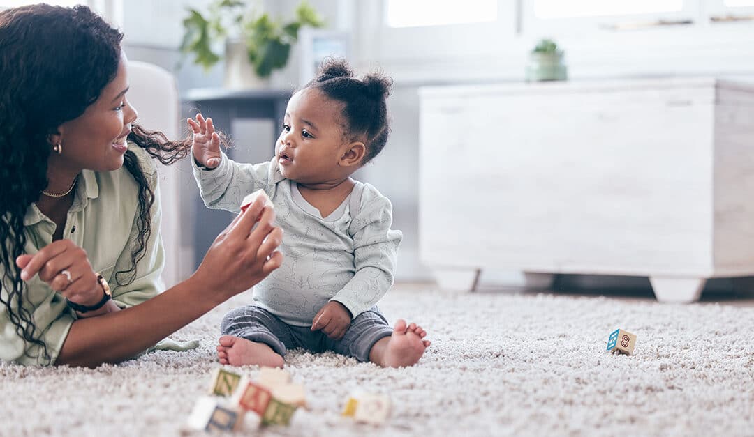 Baby, mother and toy letter blocks for language acquisition and development on living room floor.