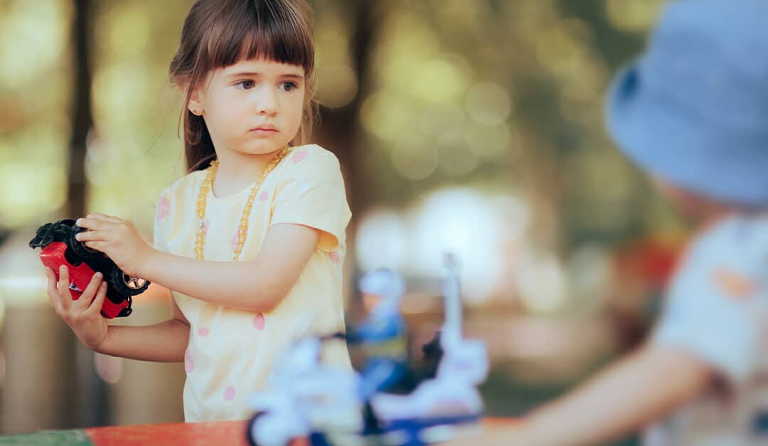 Little girl holding a toy while playing with a little boy, learning how to ask in Spanish “¿Es tuyo?” or "Is it yours?"