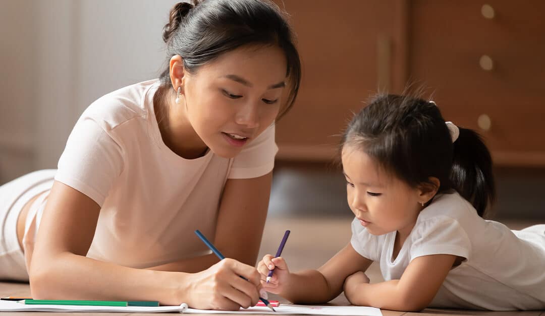 Smiling Asian mother lying on floor with young daughter teaching language