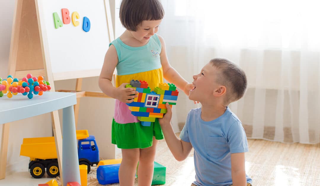 A boy and a girl are holding a heart made of plastic blocks learning to share and also say it's mine