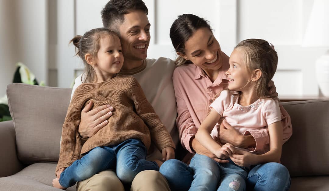 Mother and father on couch holding their two daughter on their laps, bilingual parenting