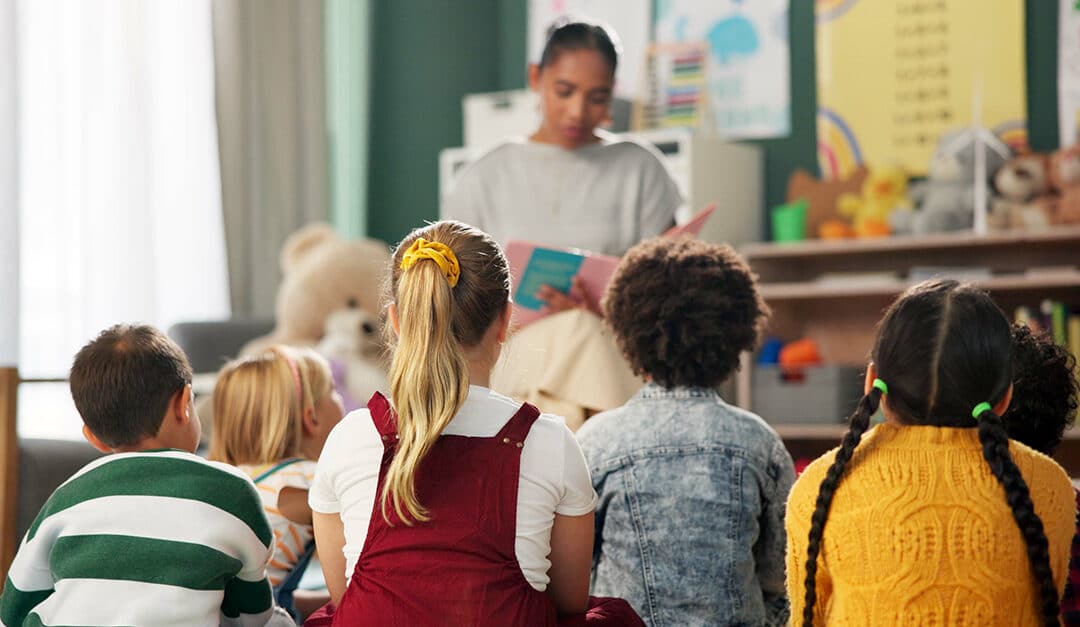 Young children in a classroom, sitting on the floor listening to their teacher reading in a dual language program