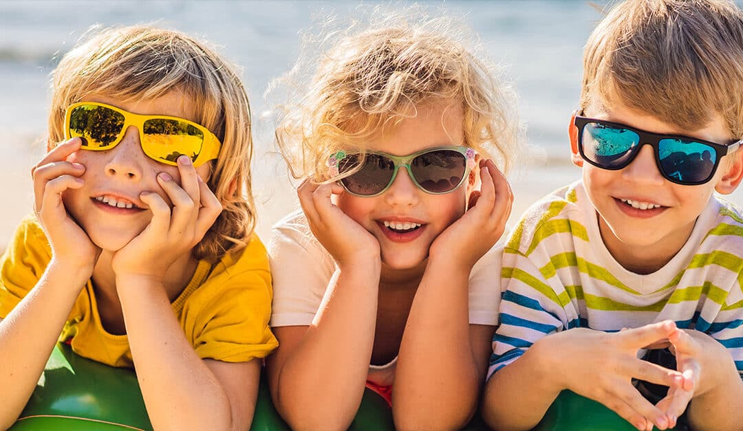 Three young kids at the beach, wearing sunglasses and smiling at the camera, illustrating the blog topic of Spanish Vocabulary for Summer