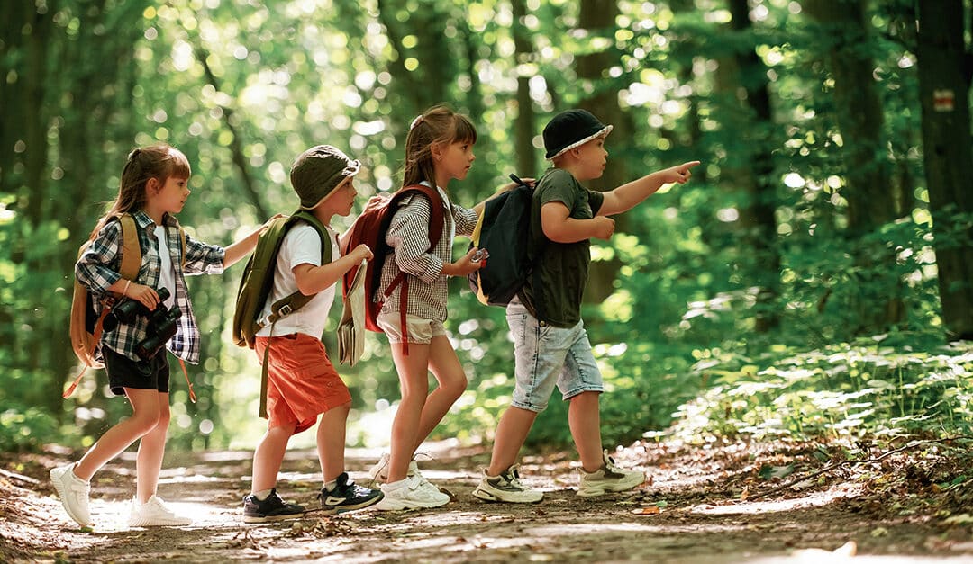 Four children hiking in the forest with backpacks, illustrating the blog topic Nature in Spanish