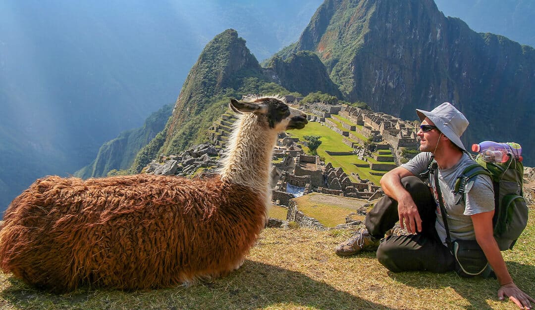 Tourist and alpaca sitting in front of Machu Picchu, Peru, illustrating the blog topic of Speaking Spanish in Peru