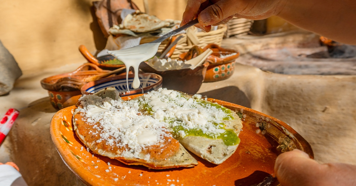 Corn tlacoyo stuffed with beans, with green sauce and red sauce, cheese, cream and onion, on a clay plate.
