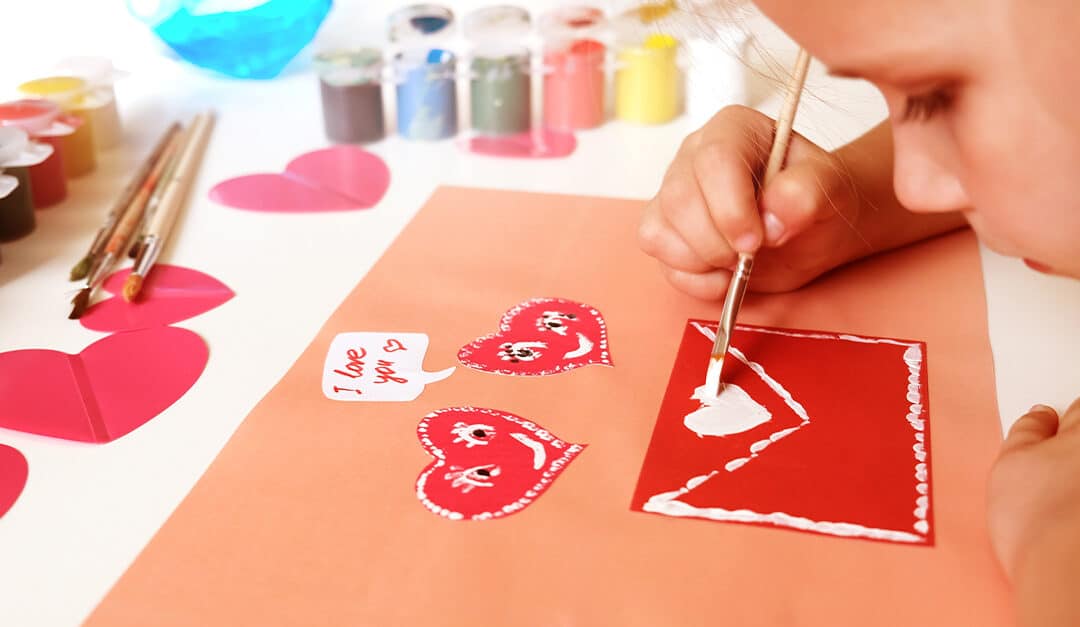 Young girl working on arts and crafts for Valentine's Day, painting a heart onto a red envelope, Illustrating the blog topic "Spanish Valentine’s Day Phrases and Vocabulary for Kids"